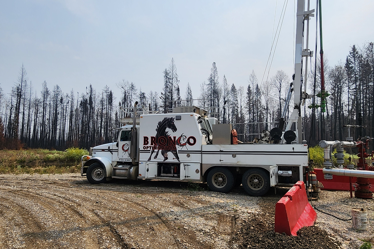 Bronco Slickline swabbing truck with mast unit in operation at an Alberta oil lease, surrounded by forested landscape—providing expert well intervention services in Drayton Valley, Grande Prairie, and Red Deer.